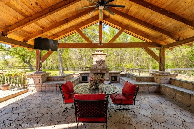 view of patio / terrace featuring a gazebo, ceiling fan, fence, an outdoor stone fireplace, and outdoor dining area