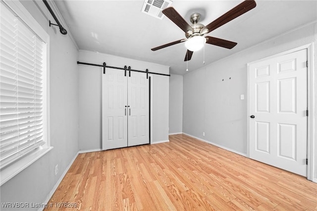 unfurnished bedroom with crown molding, light hardwood / wood-style flooring, a barn door, and ceiling fan