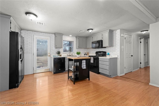 kitchen with light hardwood / wood-style flooring, a center island, black appliances, a textured ceiling, and wood counters