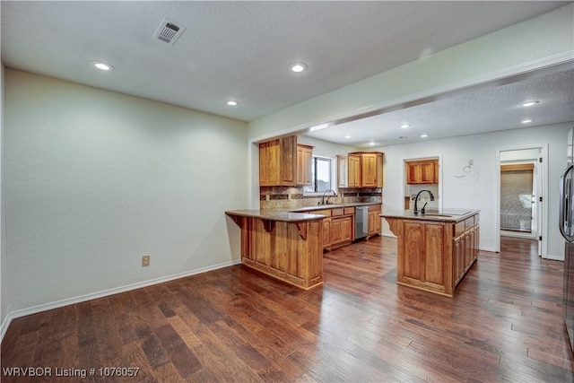 kitchen with kitchen peninsula, dark hardwood / wood-style flooring, a kitchen island with sink, sink, and dishwasher