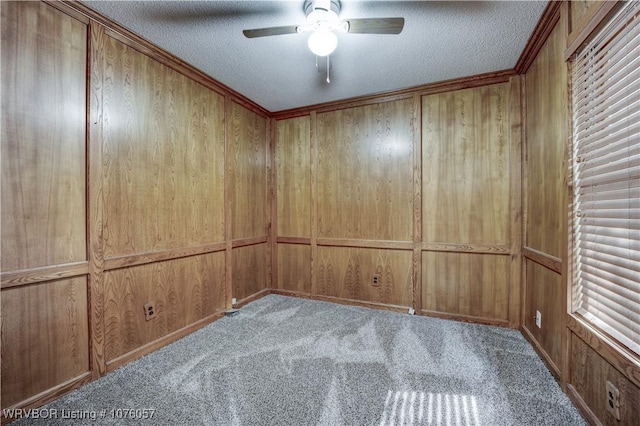 unfurnished room featuring ceiling fan, light carpet, crown molding, a textured ceiling, and wooden walls