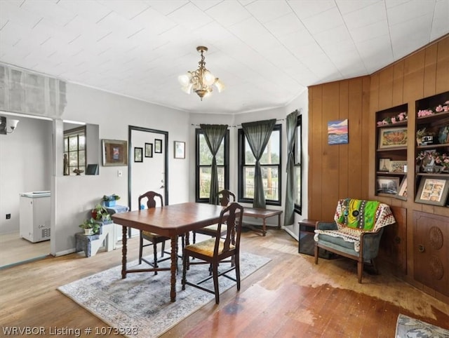 dining room with hardwood / wood-style floors, wooden walls, and a notable chandelier