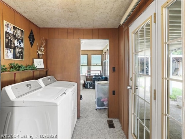 clothes washing area featuring wooden walls, washer and dryer, and light colored carpet