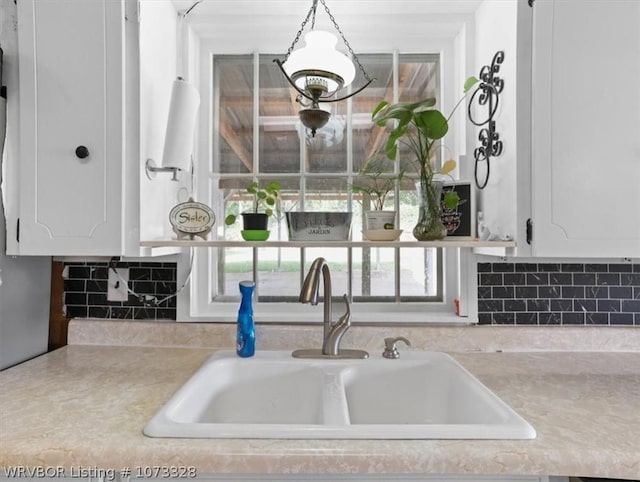 kitchen featuring white cabinets, backsplash, pendant lighting, and sink