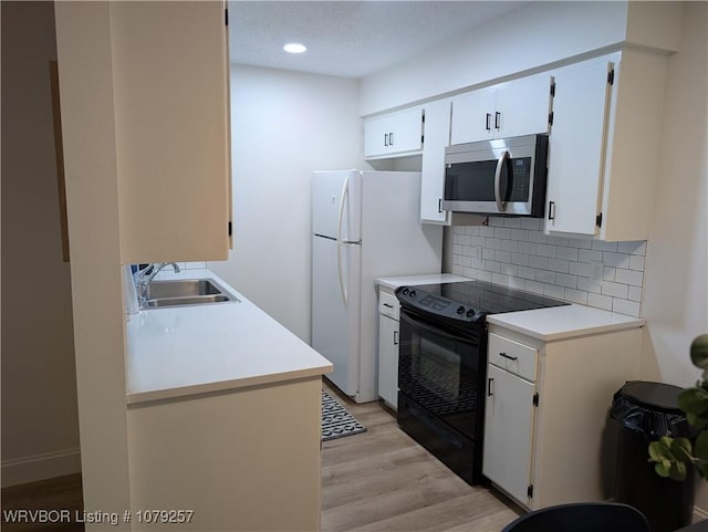 kitchen featuring light wood finished floors, tasteful backsplash, stainless steel microwave, black range with electric cooktop, and a sink