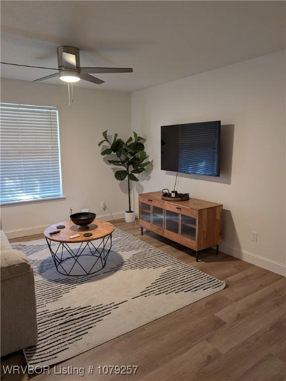 living area featuring wood finished floors, a ceiling fan, and baseboards