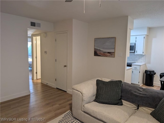 living area featuring ceiling fan, light wood finished floors, visible vents, and baseboards