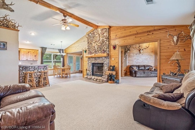 carpeted living room featuring beam ceiling, ceiling fan, a stone fireplace, high vaulted ceiling, and wooden walls