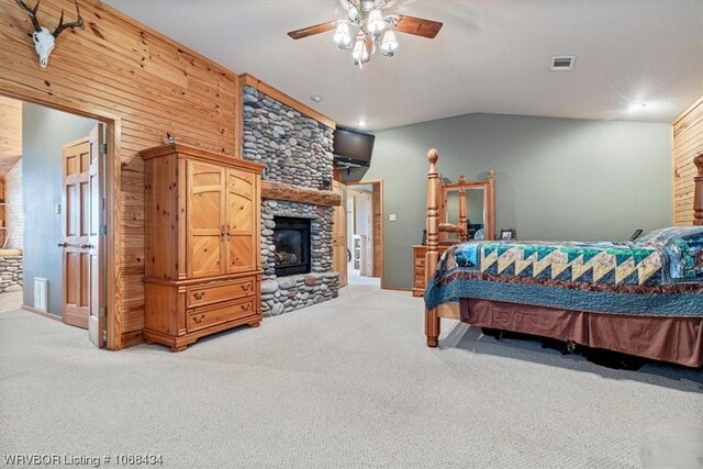 carpeted bedroom featuring a stone fireplace, wooden walls, ceiling fan, and lofted ceiling