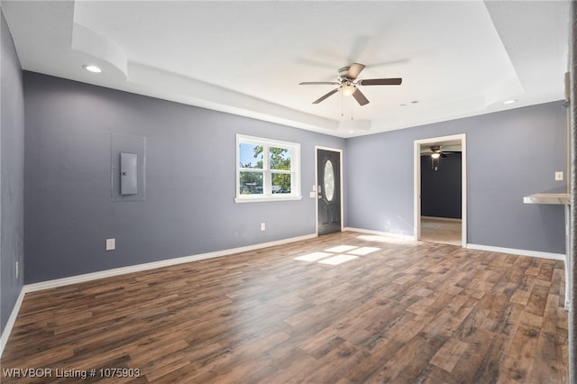 unfurnished room with a tray ceiling, electric panel, ceiling fan, and dark hardwood / wood-style floors