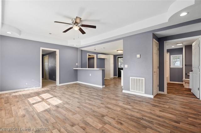 unfurnished living room with wood-type flooring, a tray ceiling, ceiling fan, and a healthy amount of sunlight