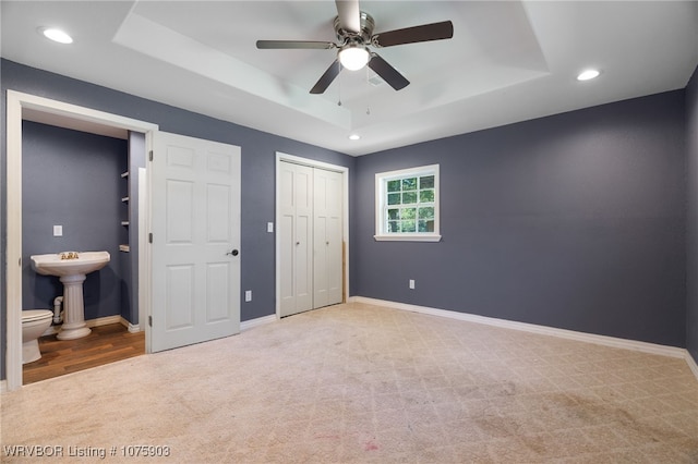 unfurnished bedroom featuring a tray ceiling, connected bathroom, ceiling fan, and light colored carpet