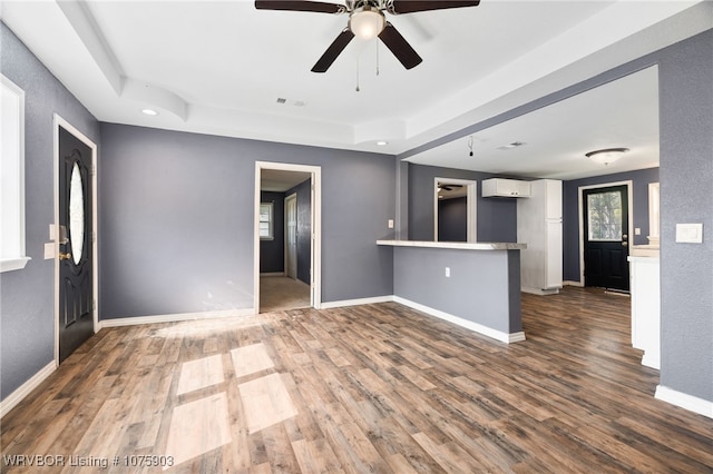 unfurnished living room featuring dark hardwood / wood-style floors, ceiling fan, and a raised ceiling