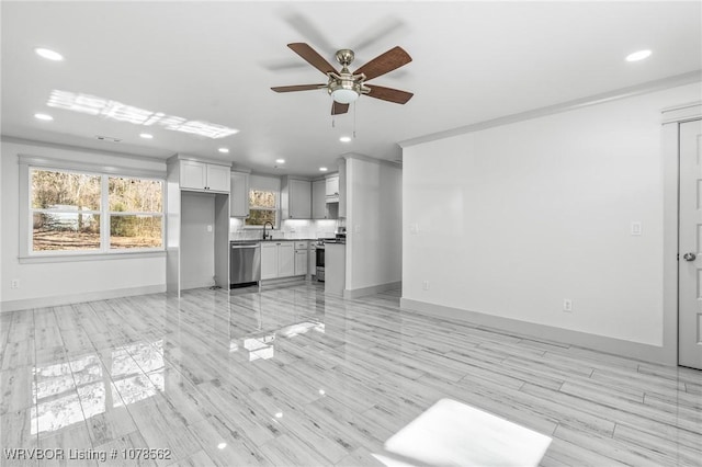 unfurnished living room with ceiling fan, sink, and ornamental molding