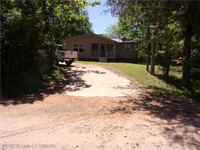 view of front of property featuring dirt driveway, a front lawn, and covered porch
