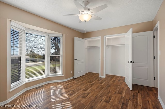 unfurnished bedroom with ceiling fan, dark hardwood / wood-style flooring, a textured ceiling, and multiple closets