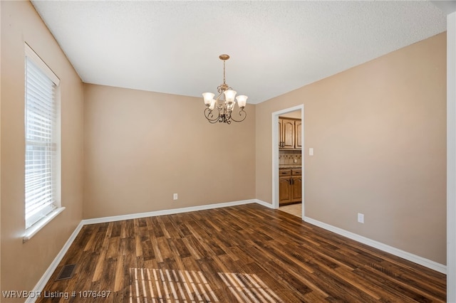 unfurnished room featuring a textured ceiling, dark hardwood / wood-style floors, and a notable chandelier