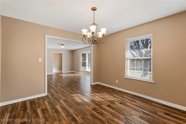 empty room with dark hardwood / wood-style floors and a notable chandelier