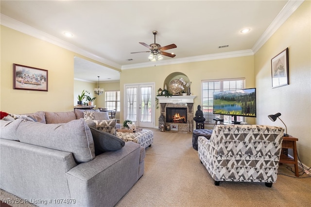 carpeted living room featuring crown molding, a stone fireplace, french doors, and ceiling fan with notable chandelier