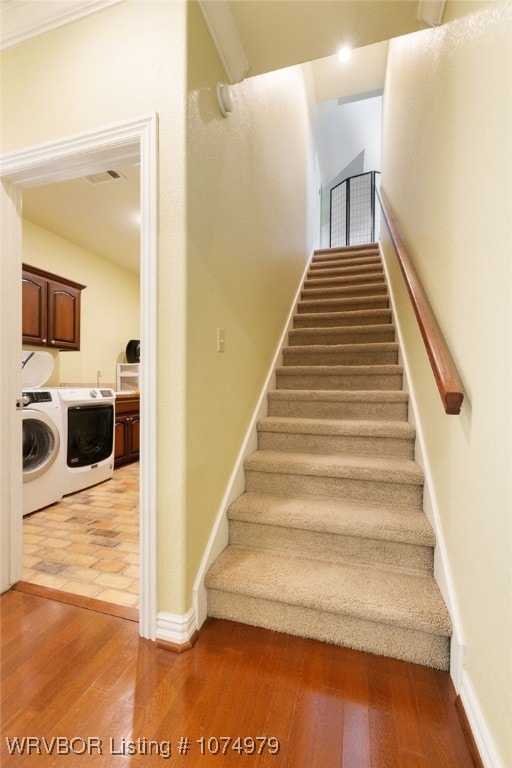 stairs with wood-type flooring, separate washer and dryer, and crown molding