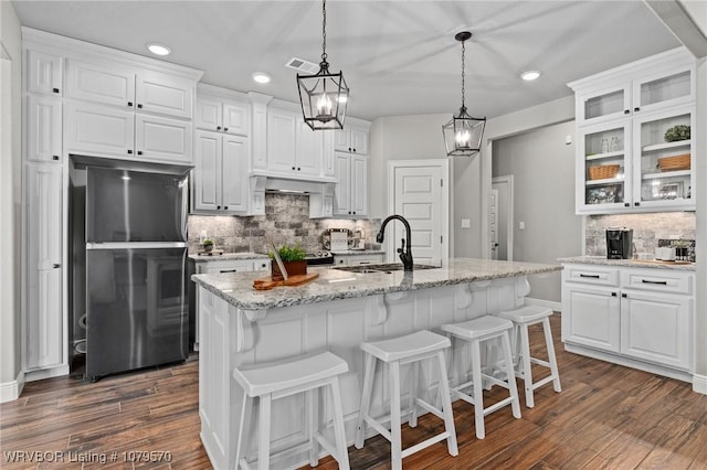 kitchen with visible vents, a sink, white cabinetry, freestanding refrigerator, and glass insert cabinets