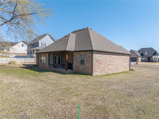 rear view of property featuring a lawn, a patio, fence, roof with shingles, and brick siding