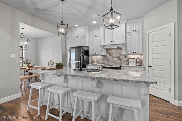 kitchen with tasteful backsplash, visible vents, dark wood-type flooring, under cabinet range hood, and a sink