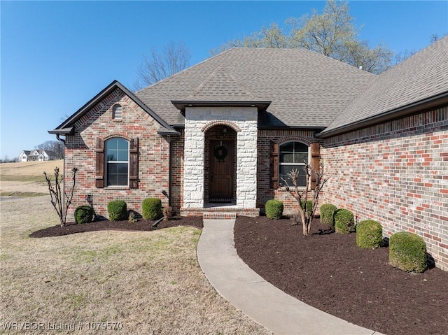 french country home featuring brick siding, a front lawn, and a shingled roof