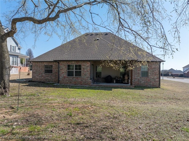 rear view of property featuring a patio, a lawn, roof with shingles, and brick siding