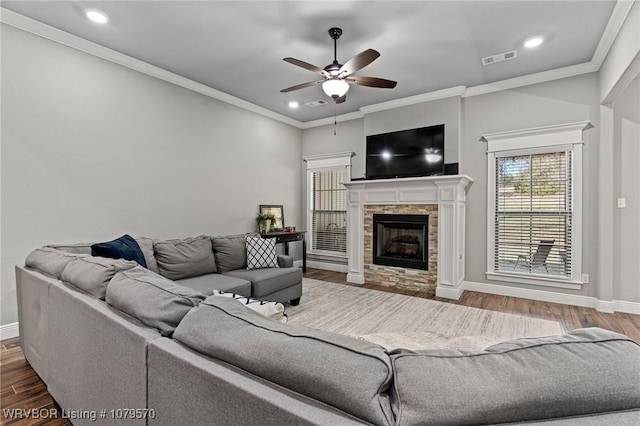 living room featuring visible vents, crown molding, baseboards, a stone fireplace, and wood finished floors