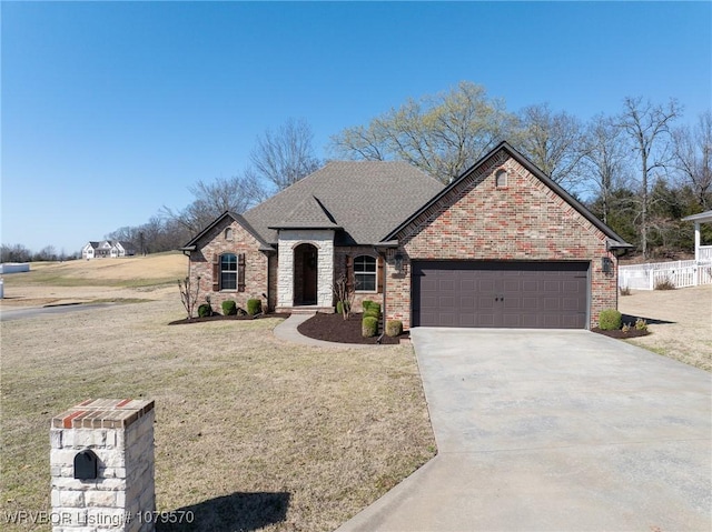 french country home with roof with shingles, a front lawn, concrete driveway, a garage, and brick siding