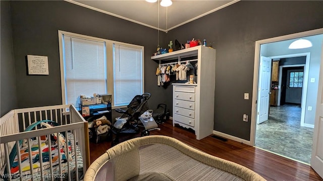 bedroom featuring a crib, crown molding, a closet, and dark wood-type flooring