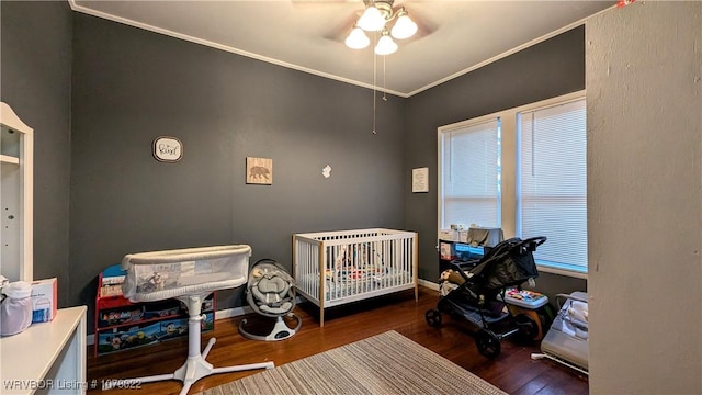 bedroom with ceiling fan, dark hardwood / wood-style flooring, ornamental molding, and a nursery area