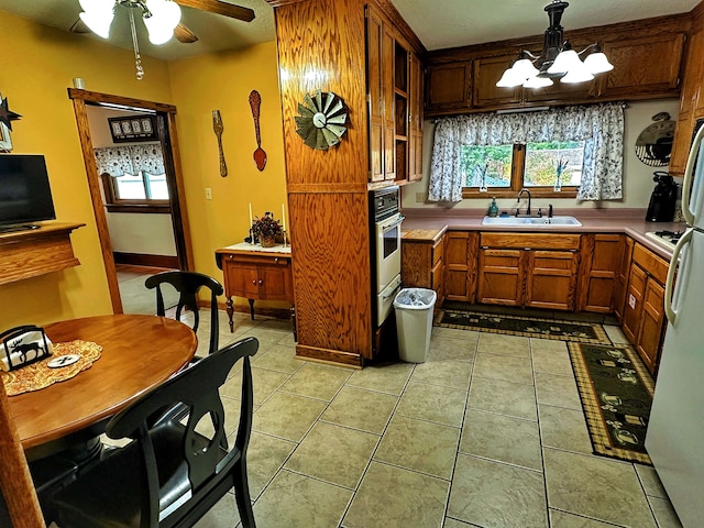 kitchen with light tile floors, decorative light fixtures, ceiling fan with notable chandelier, sink, and stainless steel oven