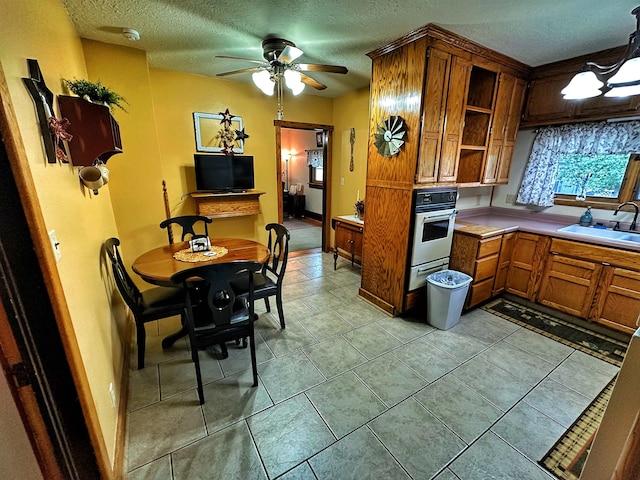 kitchen with ceiling fan, light tile floors, a textured ceiling, sink, and stainless steel double oven