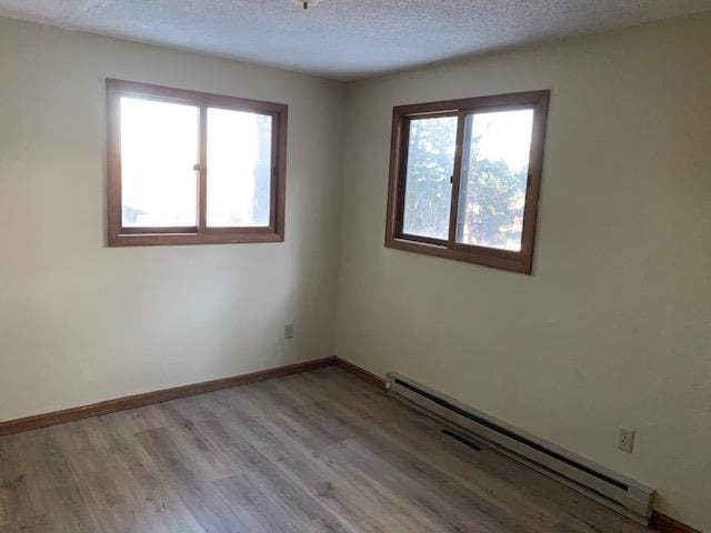 empty room featuring light wood-type flooring, baseboard heating, a textured ceiling, and a healthy amount of sunlight