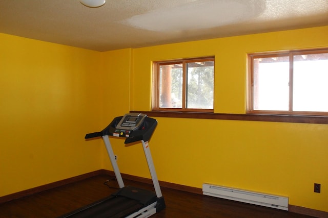 workout room featuring a healthy amount of sunlight, dark wood-type flooring, a textured ceiling, and baseboard heating