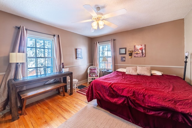 bedroom featuring ceiling fan, a textured ceiling, light wood-type flooring, and multiple windows