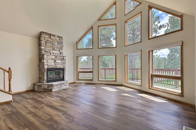 unfurnished living room featuring dark hardwood / wood-style floors, plenty of natural light, high vaulted ceiling, and a stone fireplace