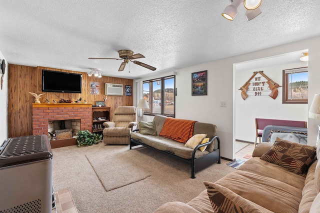 carpeted living room with wooden walls, a wall mounted air conditioner, a fireplace, ceiling fan, and a textured ceiling