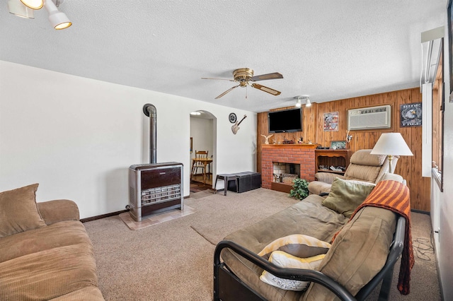 carpeted living room featuring ceiling fan, a fireplace, a textured ceiling, an AC wall unit, and wooden walls