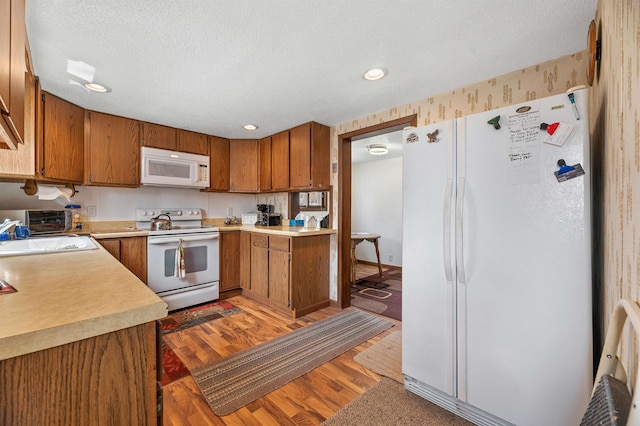 kitchen featuring sink, a textured ceiling, white appliances, and hardwood / wood-style floors