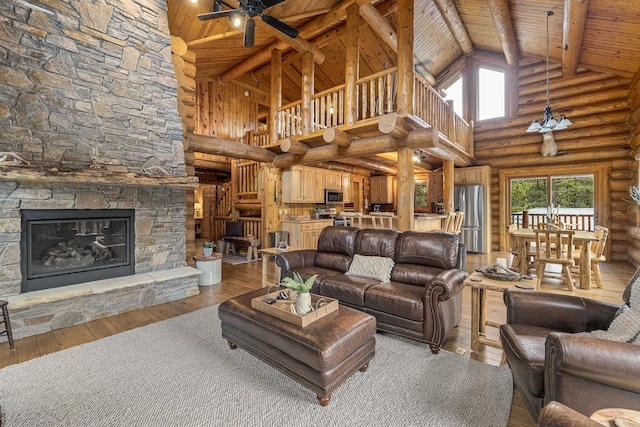 living room featuring a stone fireplace, hardwood / wood-style floors, ceiling fan, high vaulted ceiling, and beam ceiling