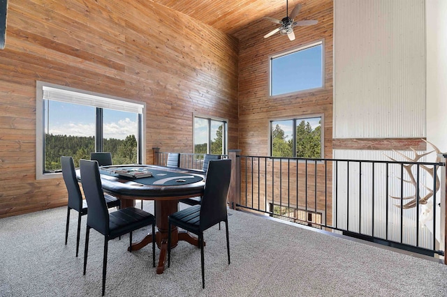 dining room featuring wood walls, carpet, a towering ceiling, wood ceiling, and ceiling fan