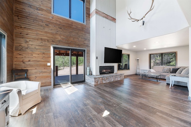 unfurnished living room featuring a wealth of natural light, wood walls, a towering ceiling, and dark hardwood / wood-style flooring