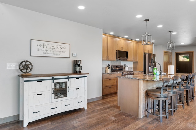 kitchen featuring stone counters, stainless steel appliances, dark hardwood / wood-style flooring, a kitchen island with sink, and pendant lighting