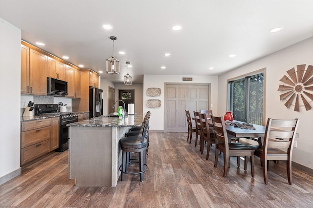 kitchen featuring gas stove, a kitchen island with sink, refrigerator with ice dispenser, and dark wood-type flooring