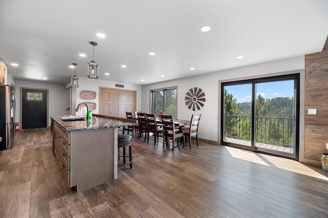 kitchen featuring dark hardwood / wood-style flooring, an island with sink, stainless steel refrigerator, and hanging light fixtures