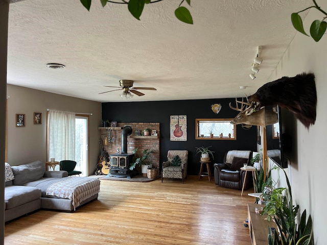 living room featuring a wood stove, a textured ceiling, hardwood / wood-style flooring, ceiling fan, and track lighting