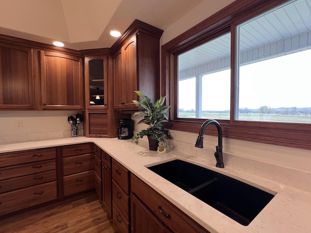 kitchen with light stone countertops, a sink, recessed lighting, dark wood-style floors, and glass insert cabinets